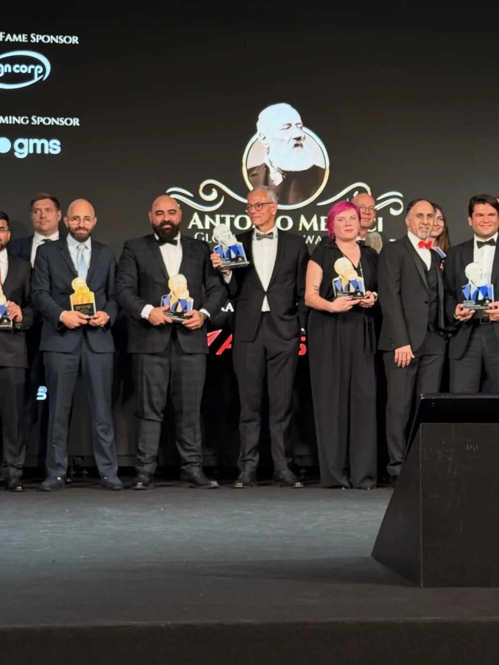 A line of award winners holding trophies on a lit stage